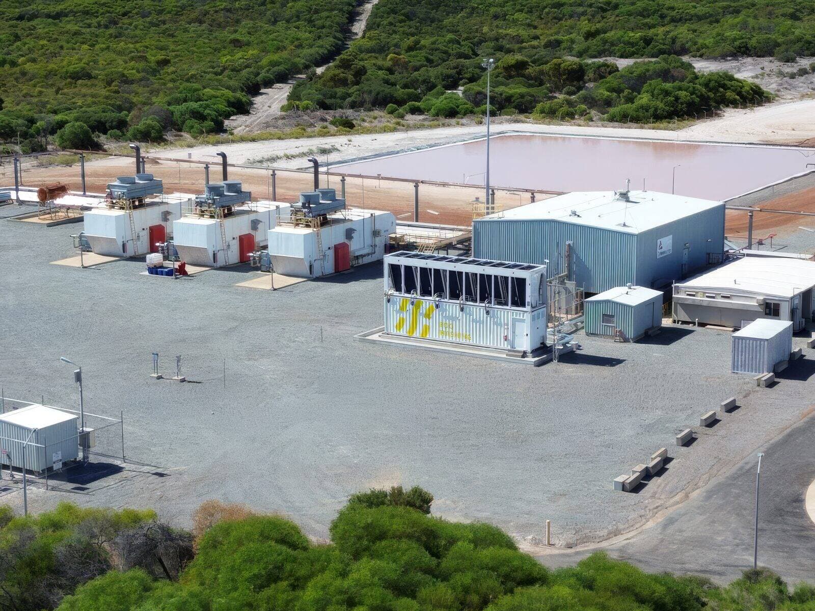 Gas-fired generator containers feeding a Fog Hashing immersion-cooled mining container beside an evaporation pond at a remote energy site.